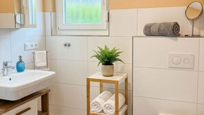 A bathroom with a white sink, a mirror, a window, a towel rack, a plant, and a towel warmer. - House Strandkrabbe, Germany (Wangerland)