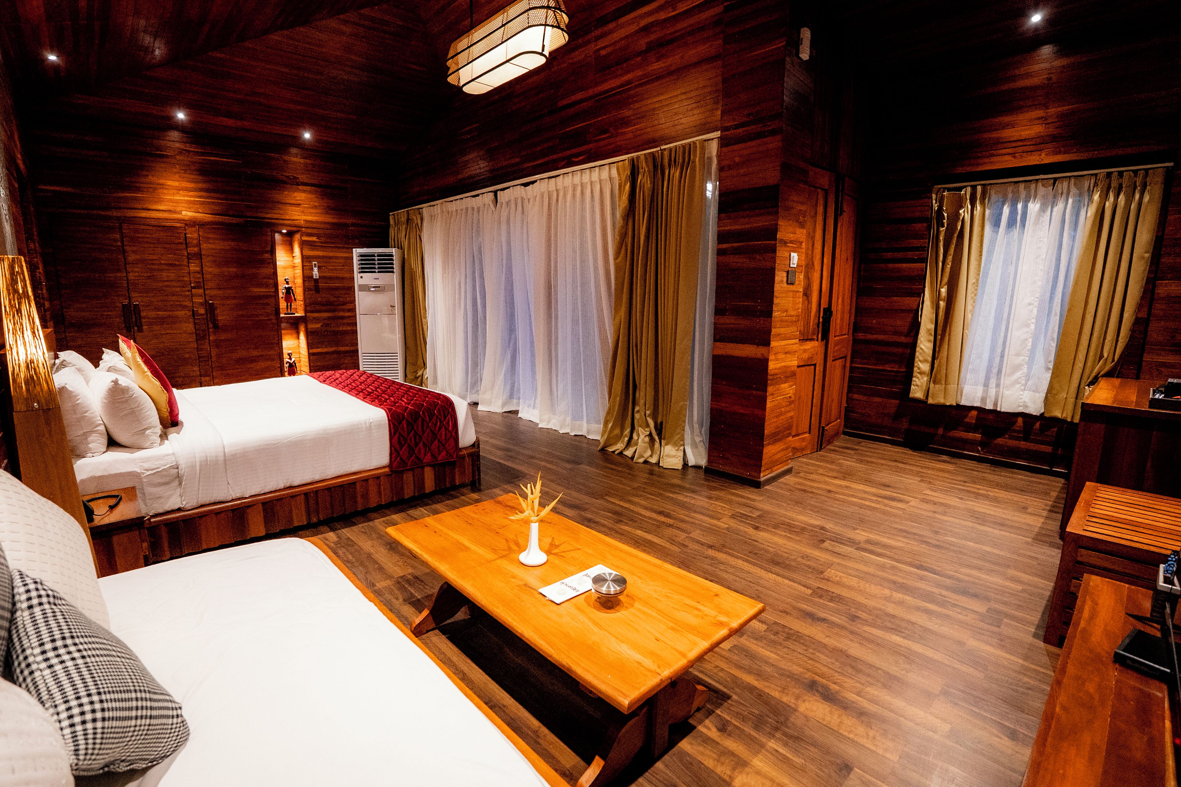 Ein Zimmer mit Holzboden, einem Bett, einer Couch, einem Holztisch und Vorhängen.
