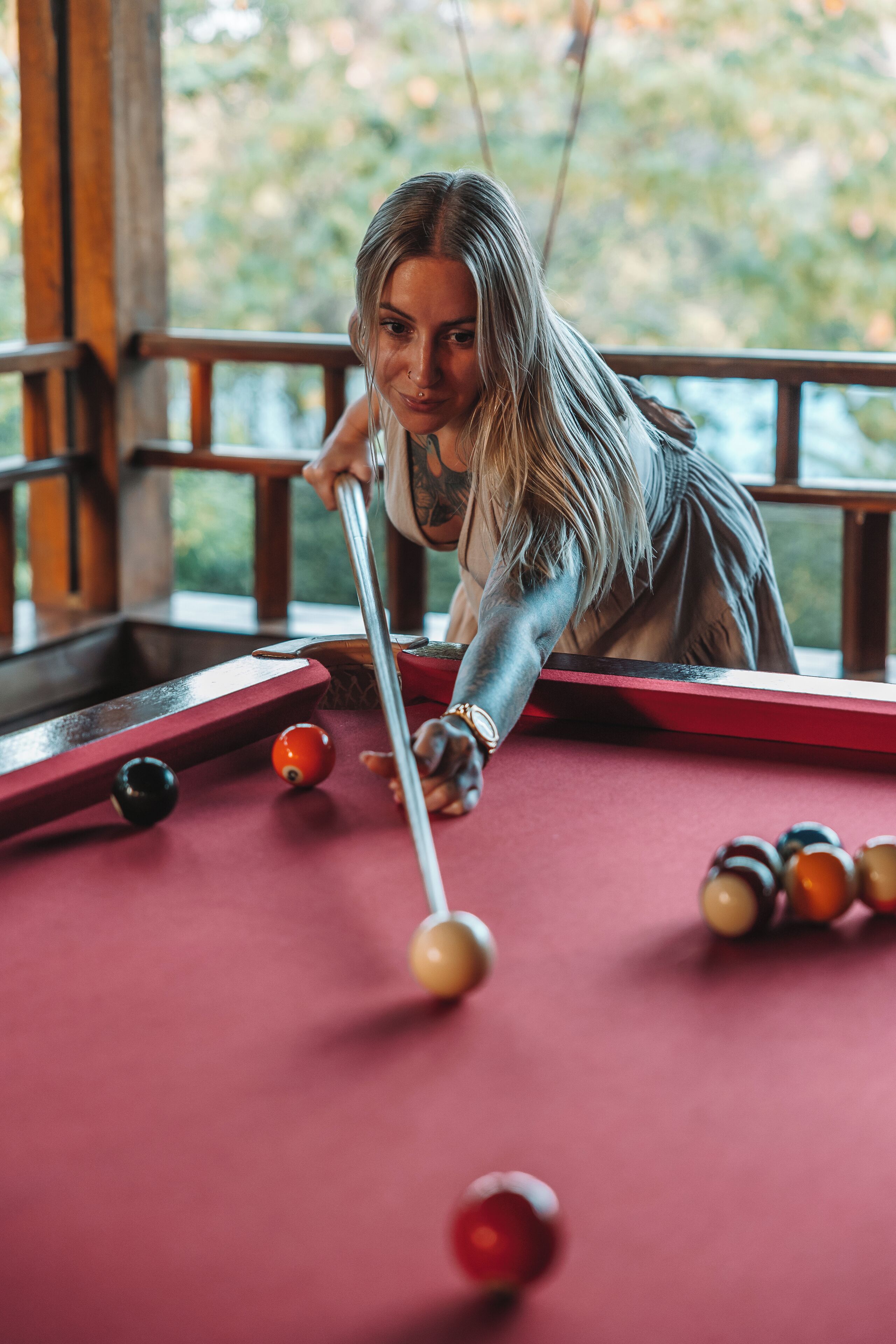Une personne joue au billard sur une table dotée d’une rambarde en bois, avec une vue sur la verdure à l’extérieur.