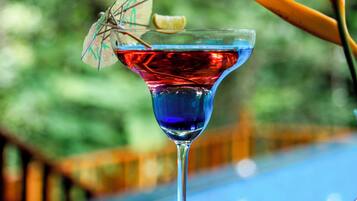 Een cocktail in een martini-glas met een decoratieve parasol op een houten tafel nabij een zwembad.