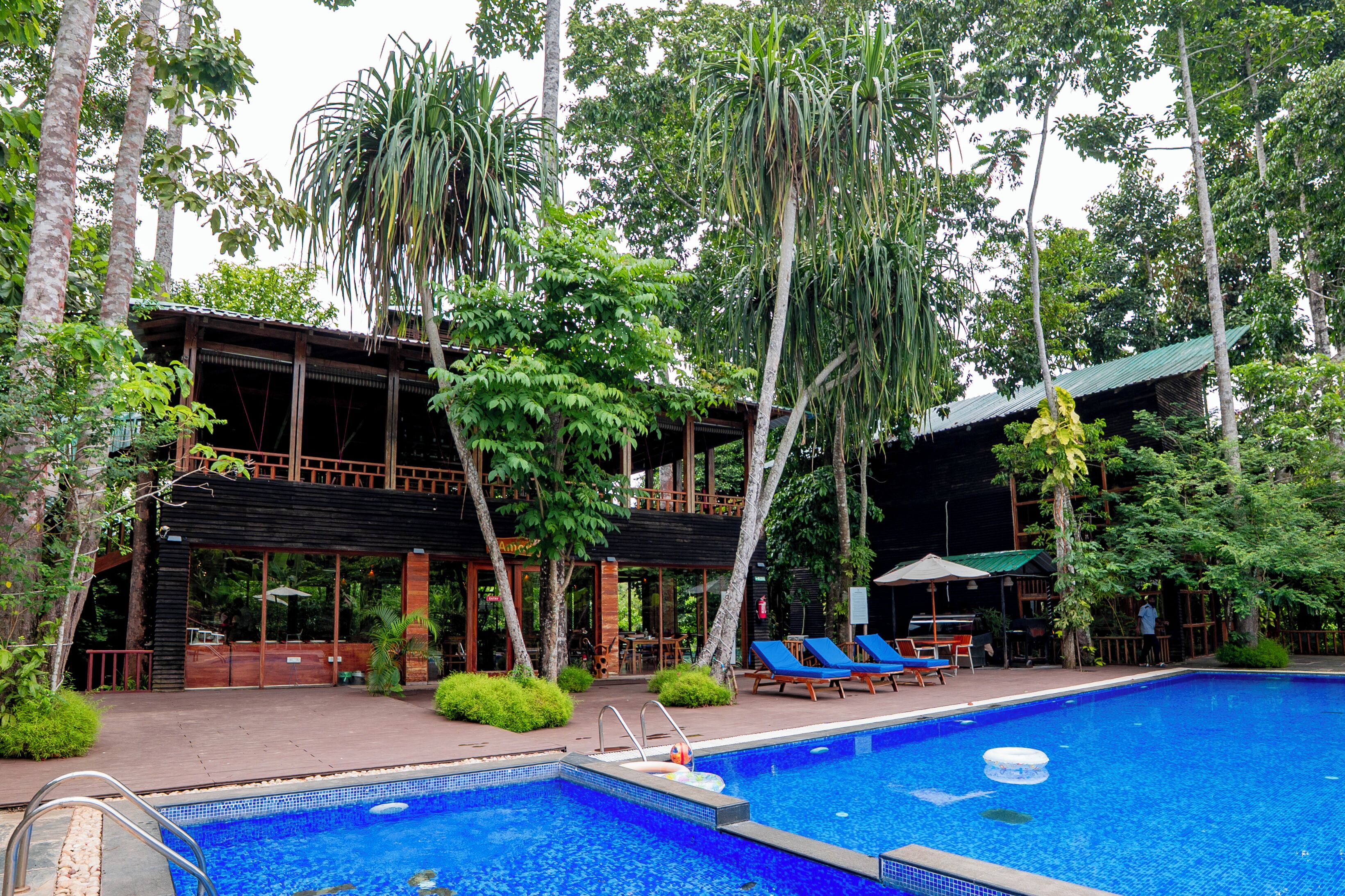 A pool area with a clear view of the pool, lounge chairs, and a building with a covered patio.