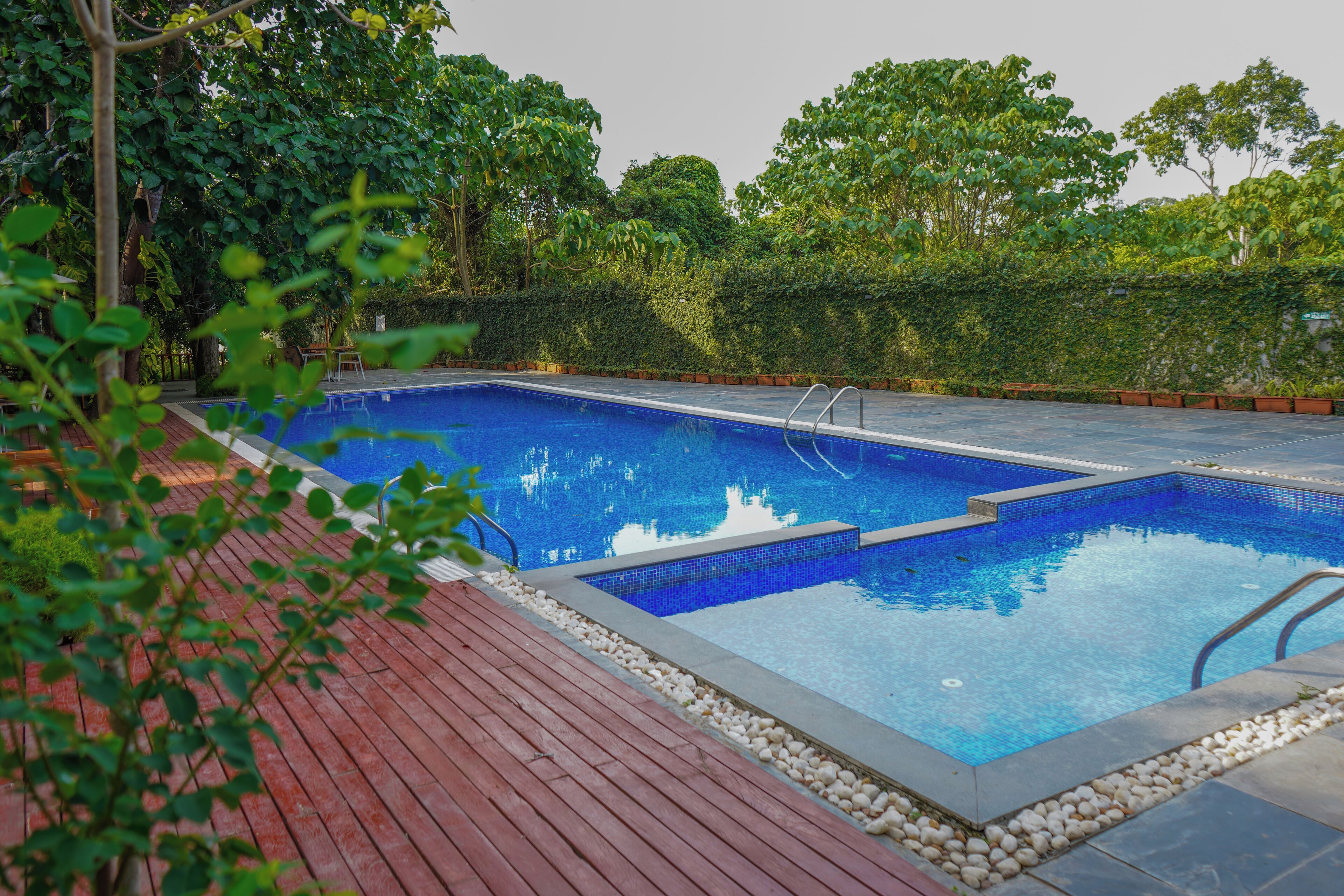 A rectangular swimming pool with a tiled edge, surrounded by a wooden deck and a low stone wall.