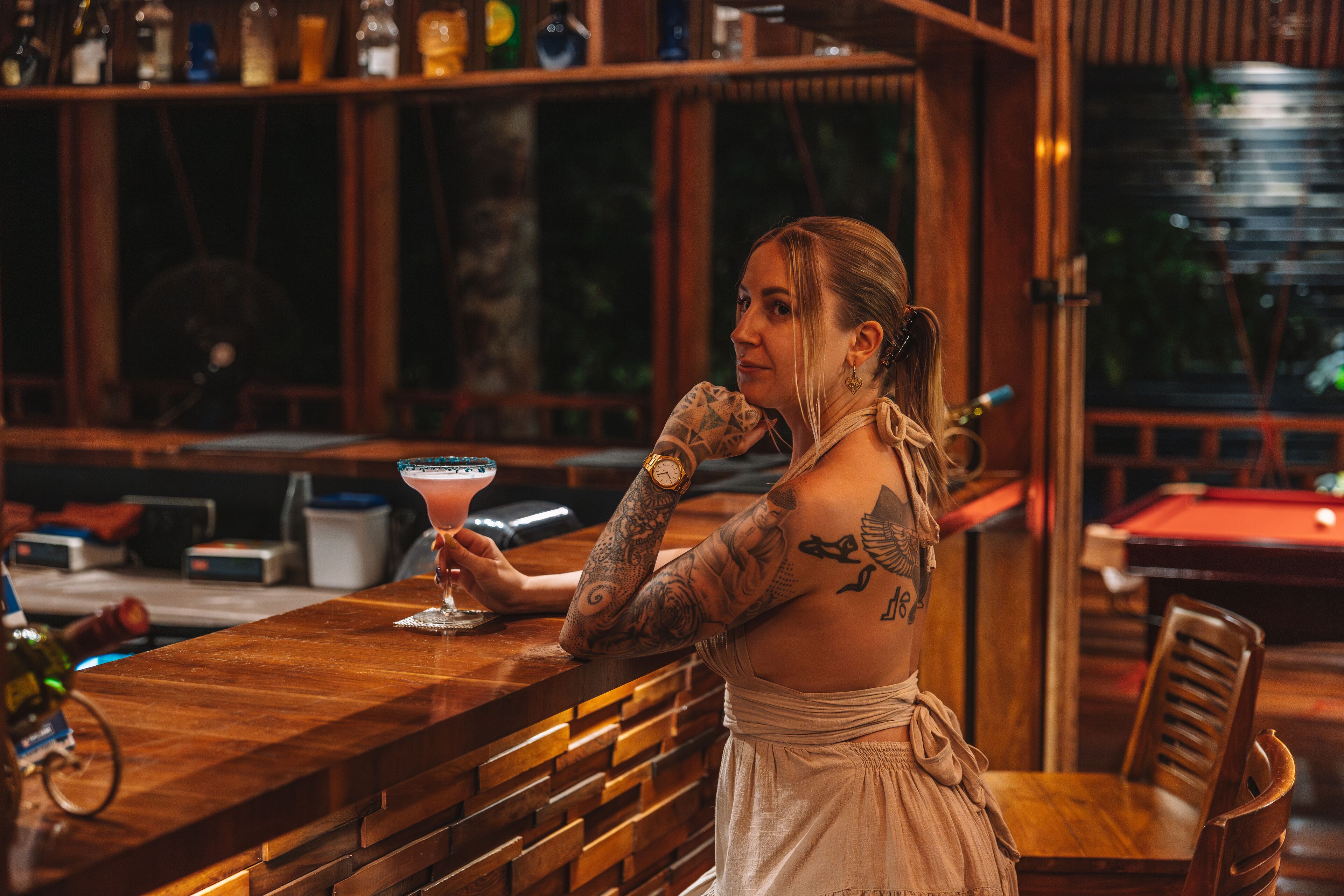 A bar area with wooden furniture, a bar counter, and a pool table in the background.