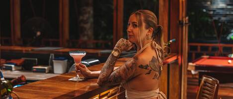 A bar area with wooden furniture, a bar counter, and a pool table in the background.