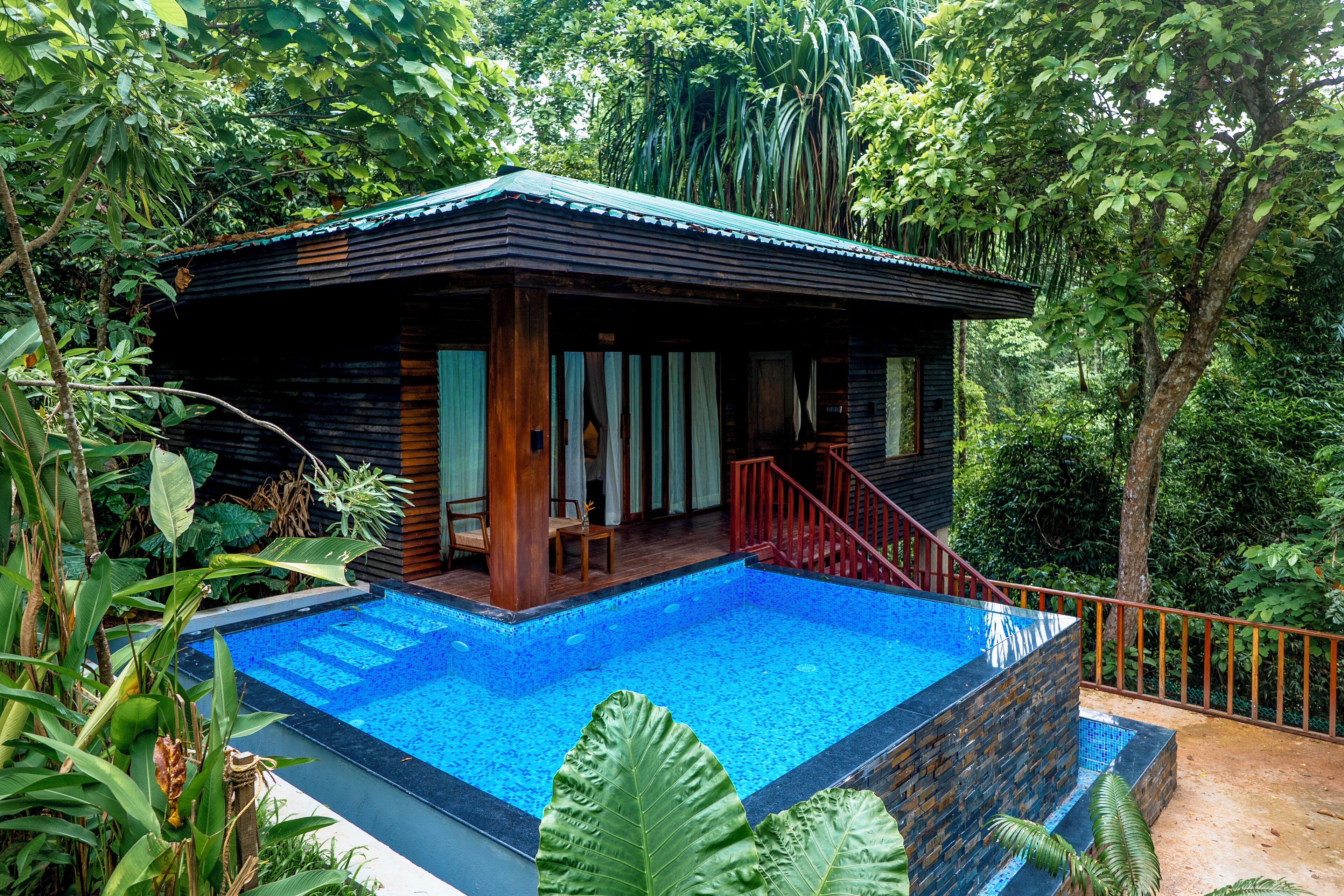 Una cabaña de madera con piscina, rodeada de exuberante follaje.