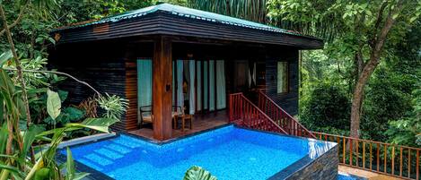 Una cabaña de madera con piscina, rodeada de exuberante follaje.