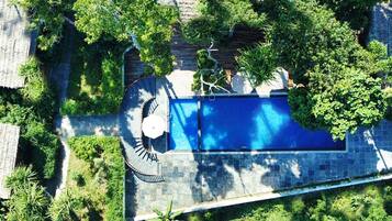 Vista aèria d'una piscina envoltada de vegetació abundant i murs de pedra.