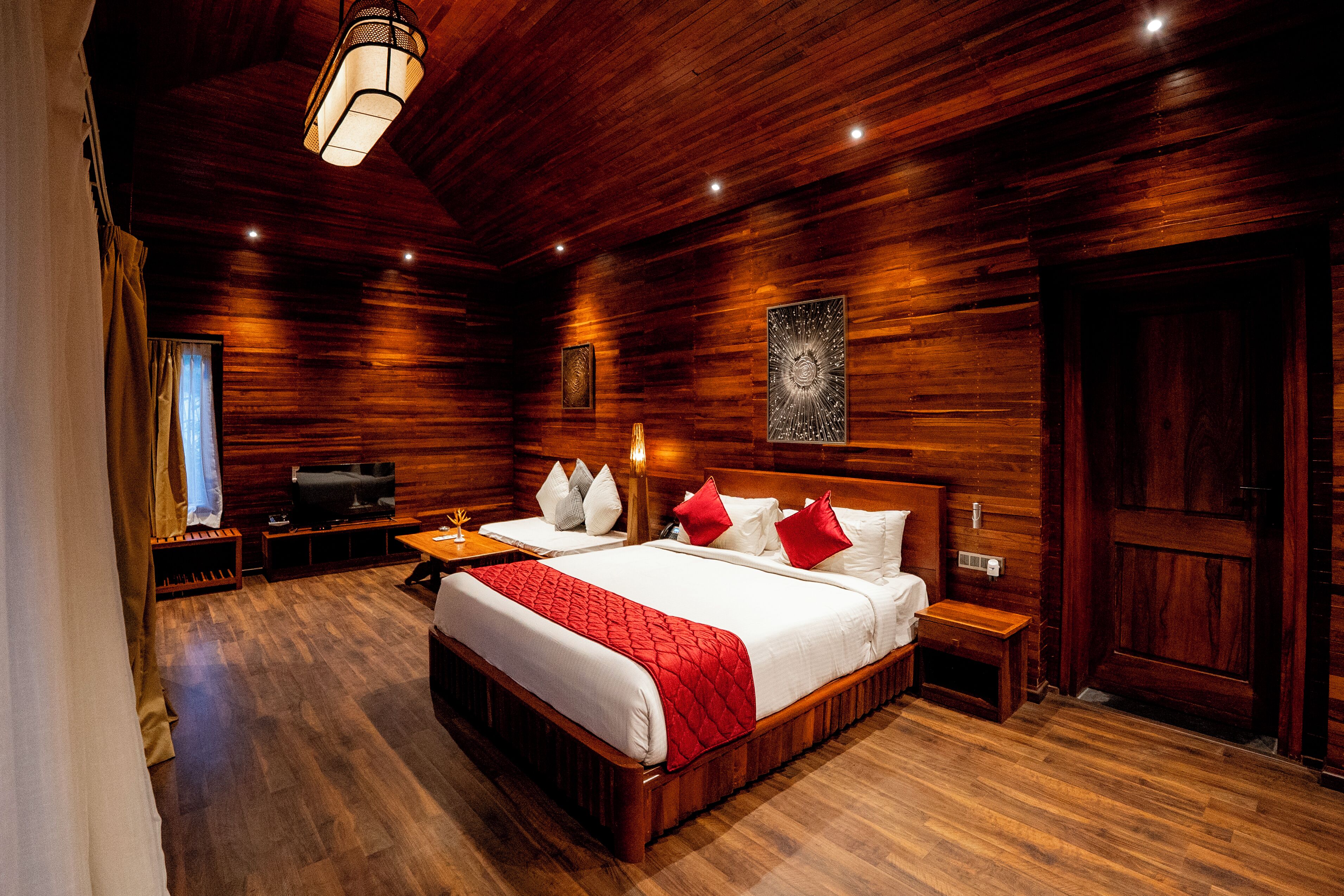 A wooden-paneled bedroom with a large bed, bedside tables, a TV, and a wooden door.