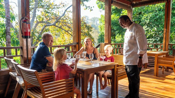 A wooden deck with a dining table and chairs, surrounded by wooden railings and trees. - De Foret (Port Blair)