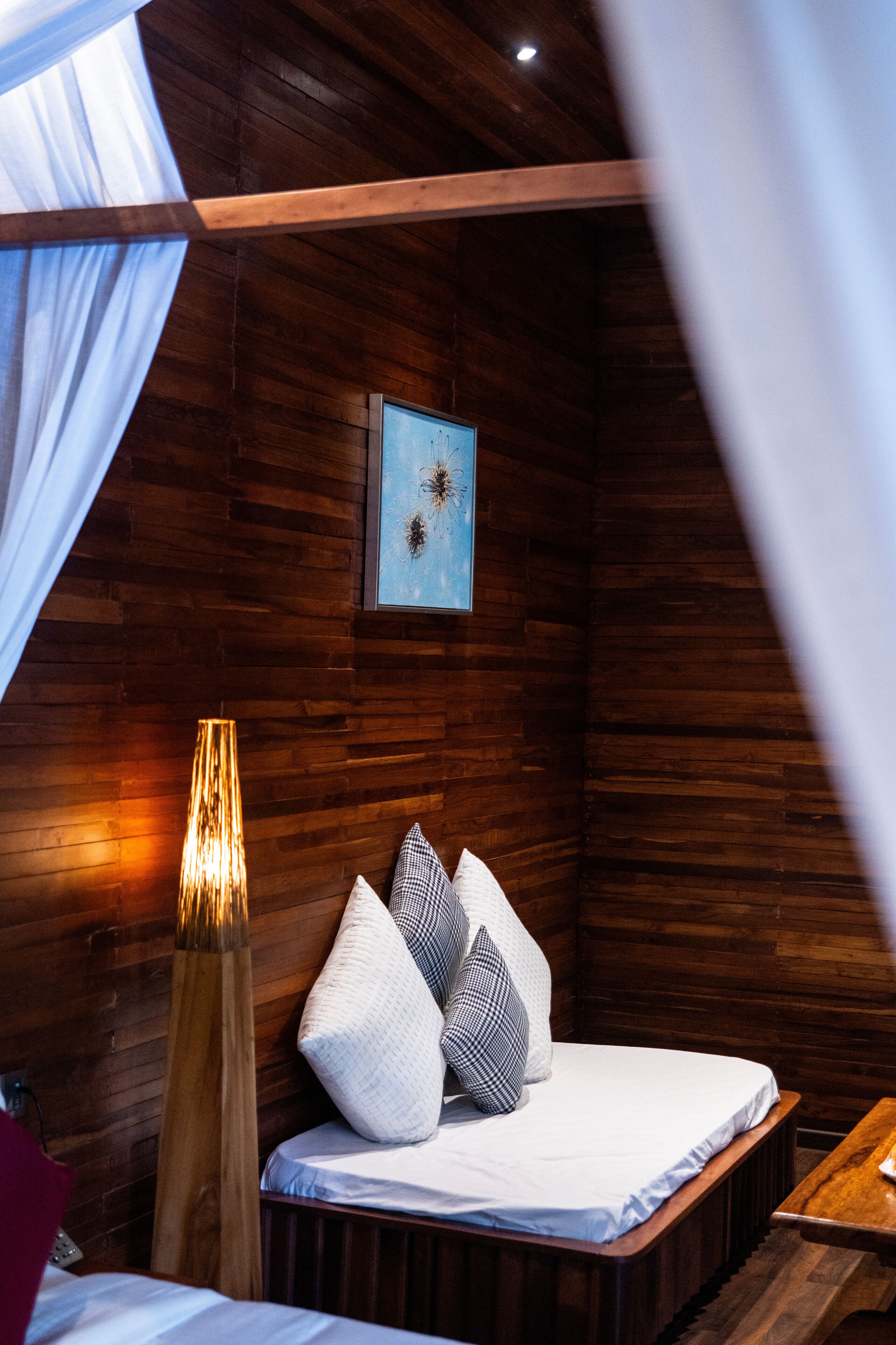 Une chambre confortable avec un plafond en bois, un lit avec des oreillers, une lampe de chevet et un tableau encadré au mur.