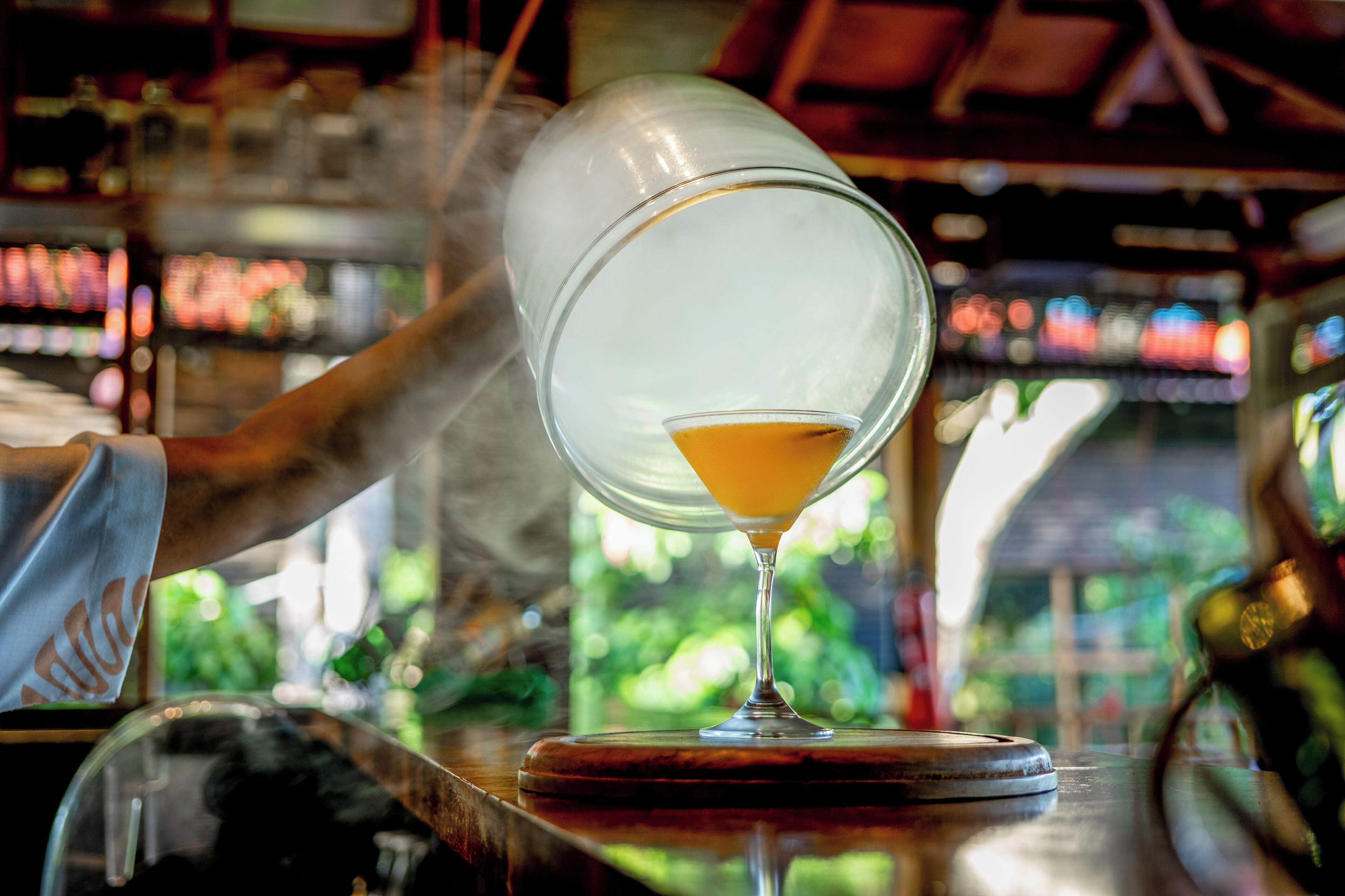 A bar setting with a clear glass of amber liquid, a bar counter, and shelves with bottles in the background.