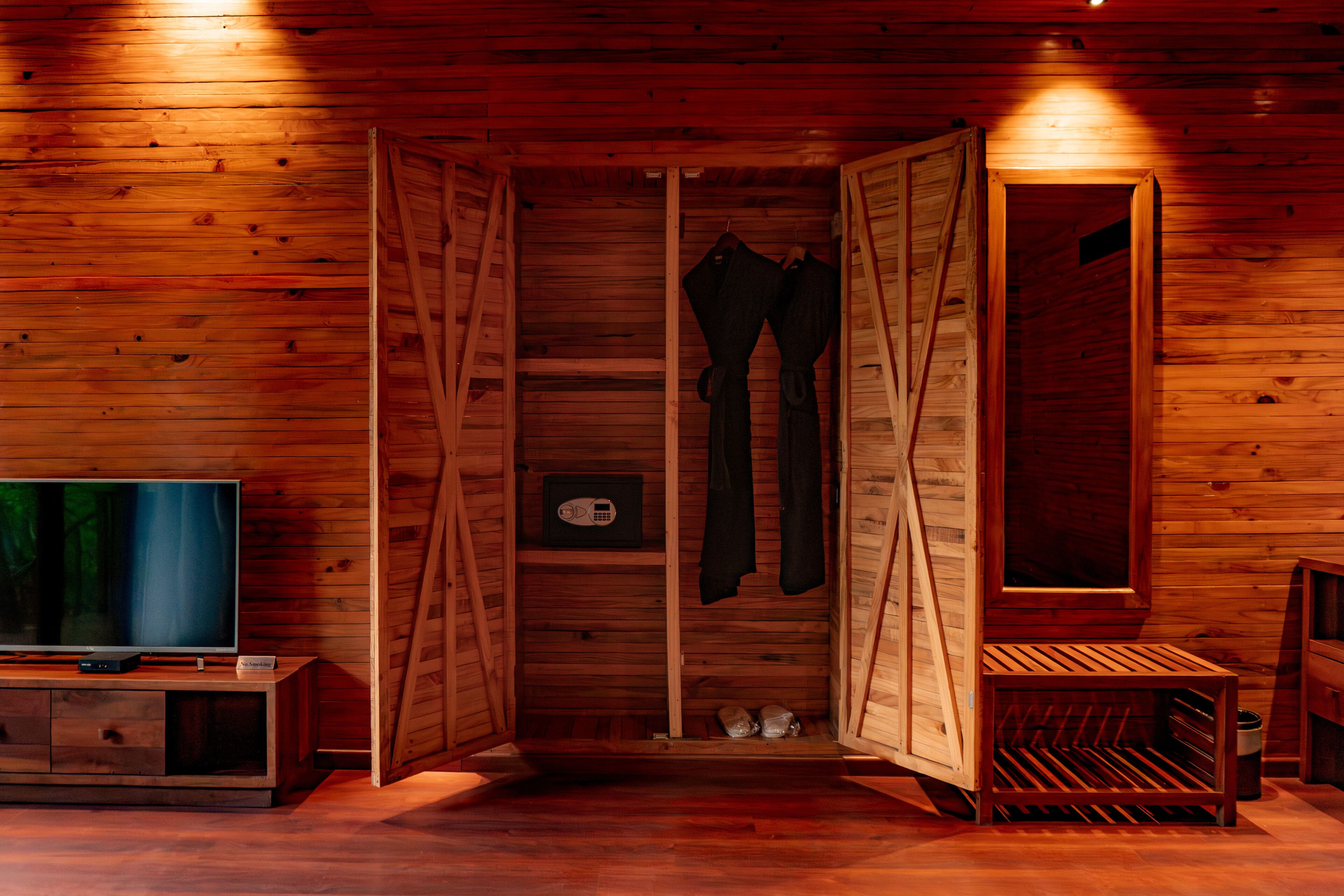 A wooden cabin interior with a television, a shoe rack, and a bench.