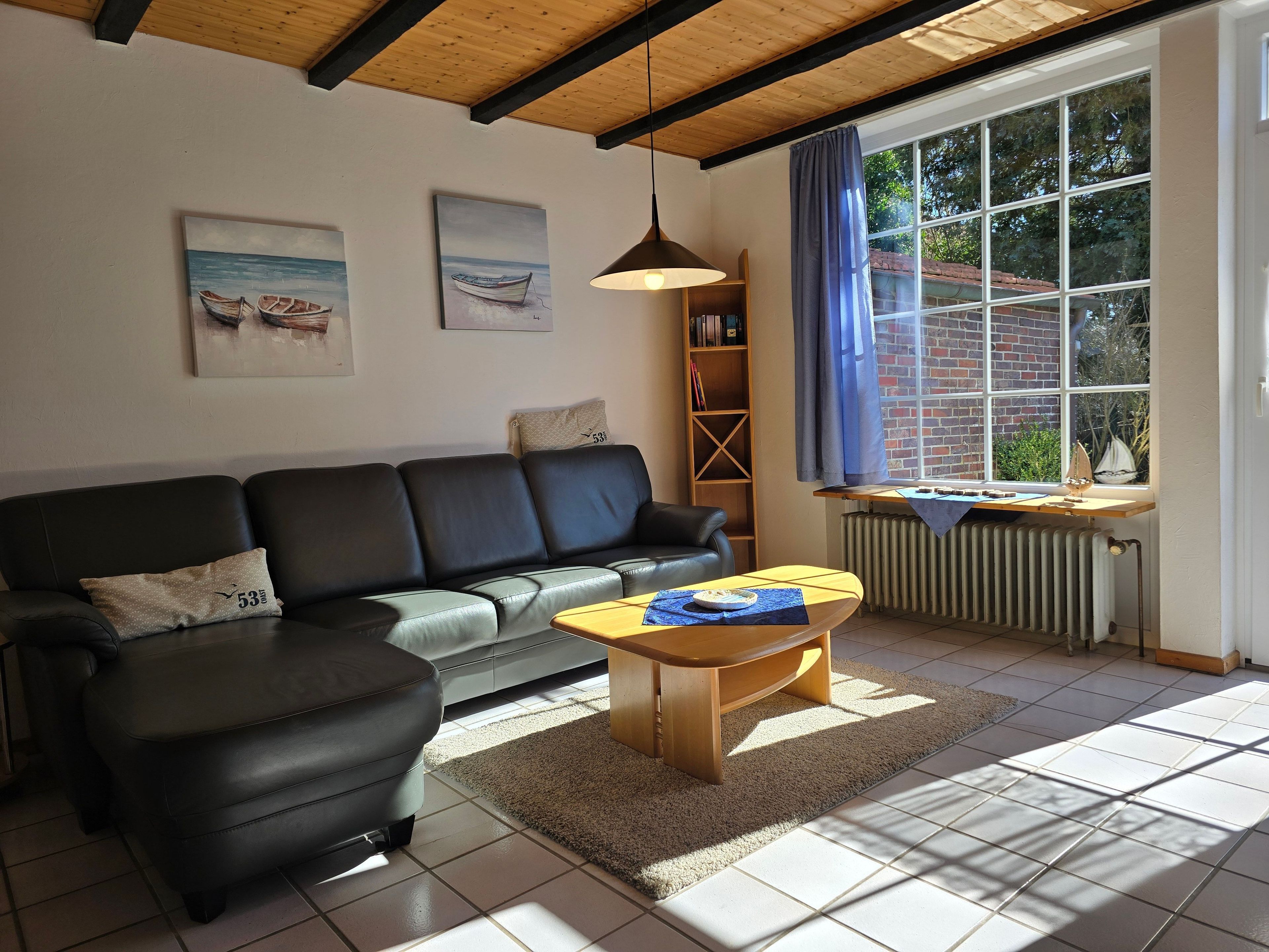 A living room with a sofa, a coffee table, a bookshelf, and a large window with a view of greenery.