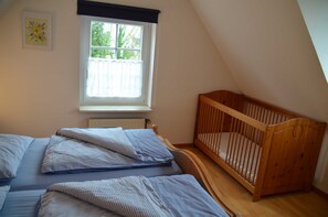Et soveværelse med en rejsebarneseng, et vindue med udsigt til træer og en radiator.