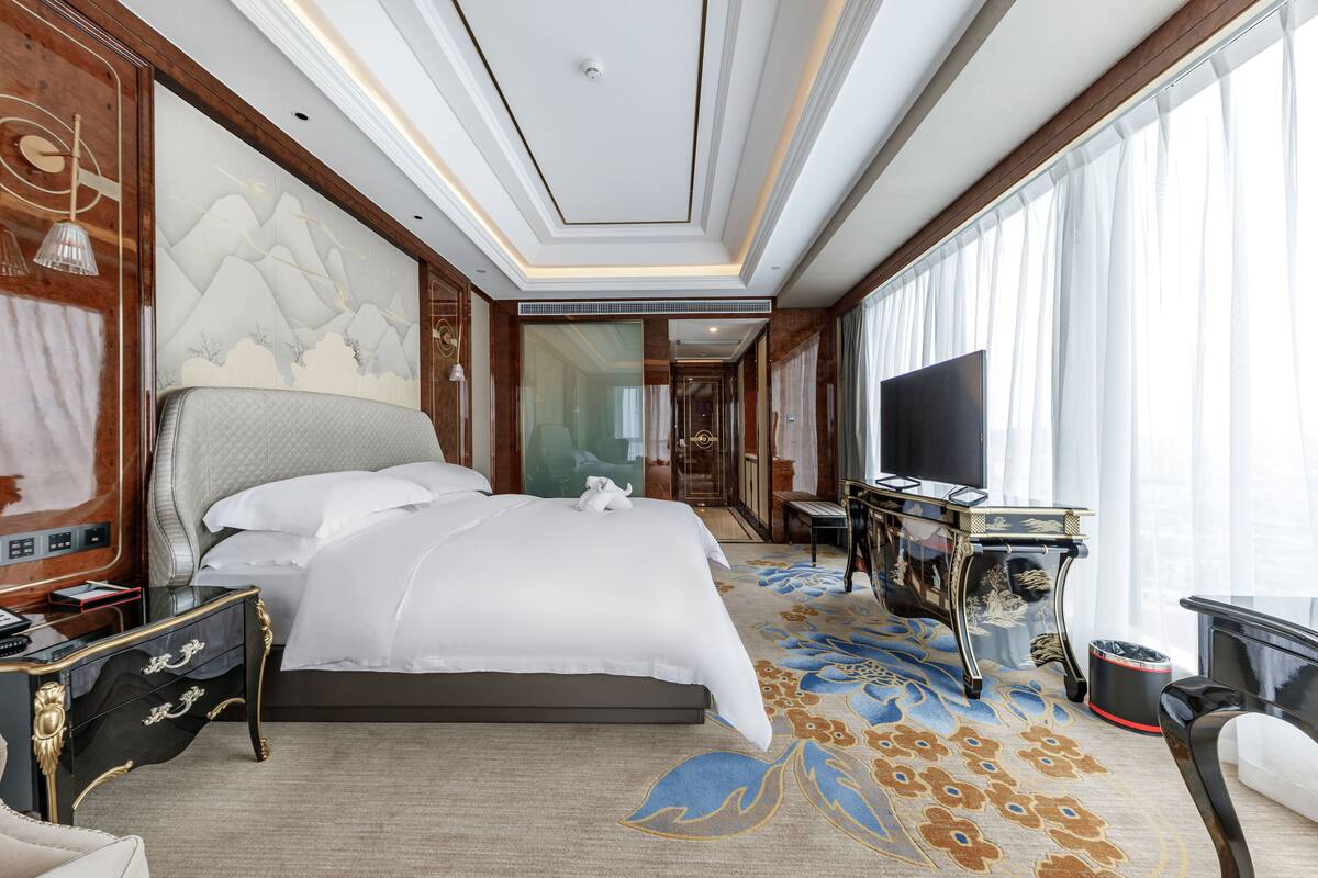 Quarto de hotel espaçoso com uma cama grande, uma escrivaninha e televisão de tela plana, e piso coberto de carpete.
