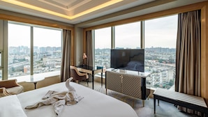 Habitación de hotel con una cama grande, un escritorio, un televisor y vistas a la ciudad.