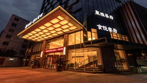 Entrada de hotel con fachada de vidrio, área de acceso techada y señalización de servicios.