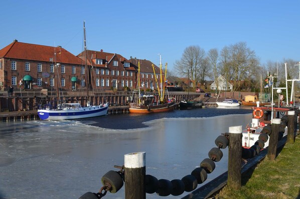 A canal with boats, a wooden fence, and a brick building with a red roof. - House Peter, Germany (Wangerland)