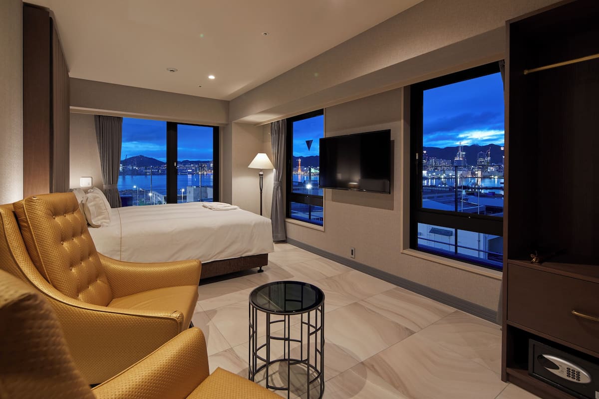 A modern hotel room with a large bed, a sitting area with a chair, a small table, and a TV.
