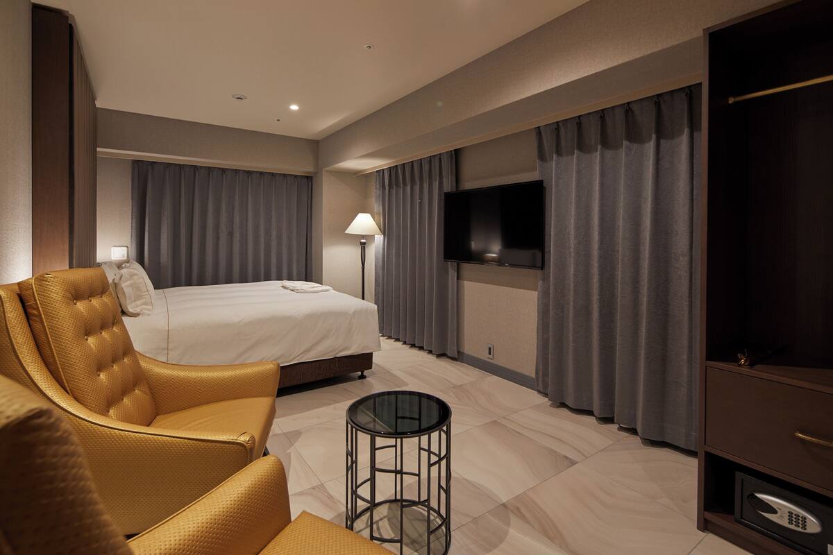 A hotel room with a bed, a sofa, a TV, a lamp, and a small table.