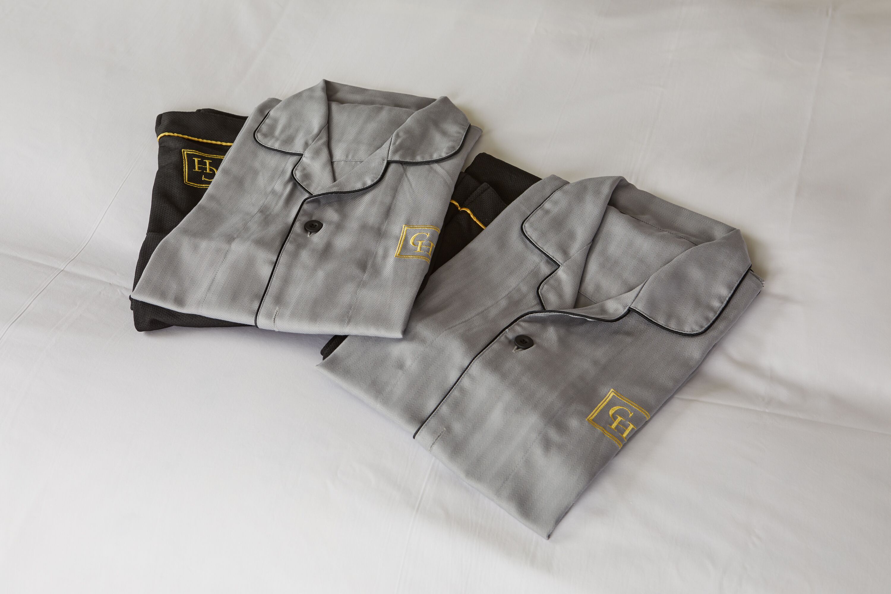 Two neatly folded grey shirts with a logo on the chest, placed on a white bed.