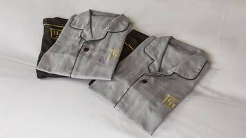 Two neatly folded grey shirts with a logo on the chest, placed on a white bed.