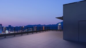 A rooftop terrace with a metal railing, a tiled floor, and a view of city buildings and mountains in the background. - Centurion Hotel & Spa Vintage Kobe (Kobe)