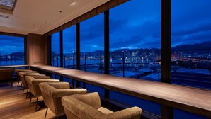 A modern hotel room with a long wooden bar, several cushioned chairs, and large windows offering a city view. - Centurion Hotel & Spa Vintage Kobe (Kobe)