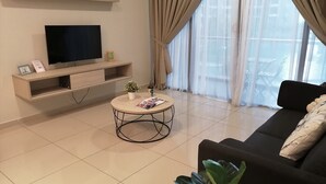 A modern living room with a flat-screen TV, a round coffee table, a sofa, and a large window with sheer curtains.