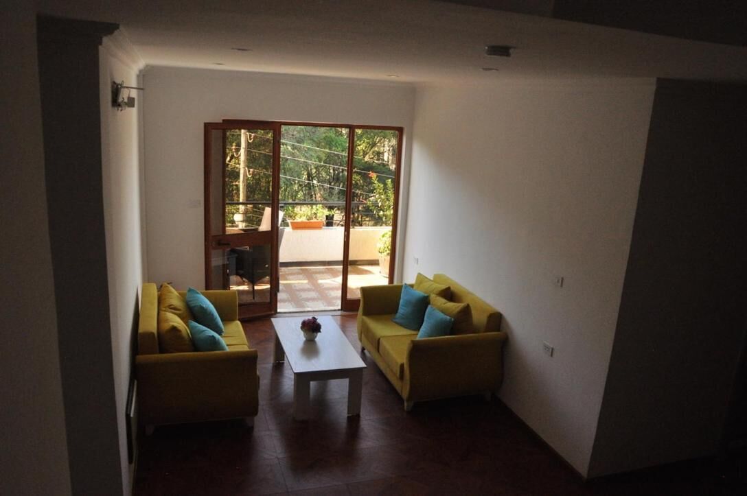 Un salón con dos sofás amarillos, una mesa de centro blanca y un ventanal corredero que da a un espacio exterior con vistas a zonas verdes.