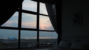 Un dormitorio con un ventanal que ofrece vistas a un horizonte urbano lejano y una masa de agua.
