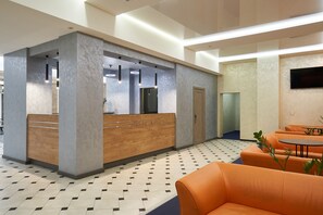 A reception area with a wooden counter, a reception desk, and seating with orange cushions.