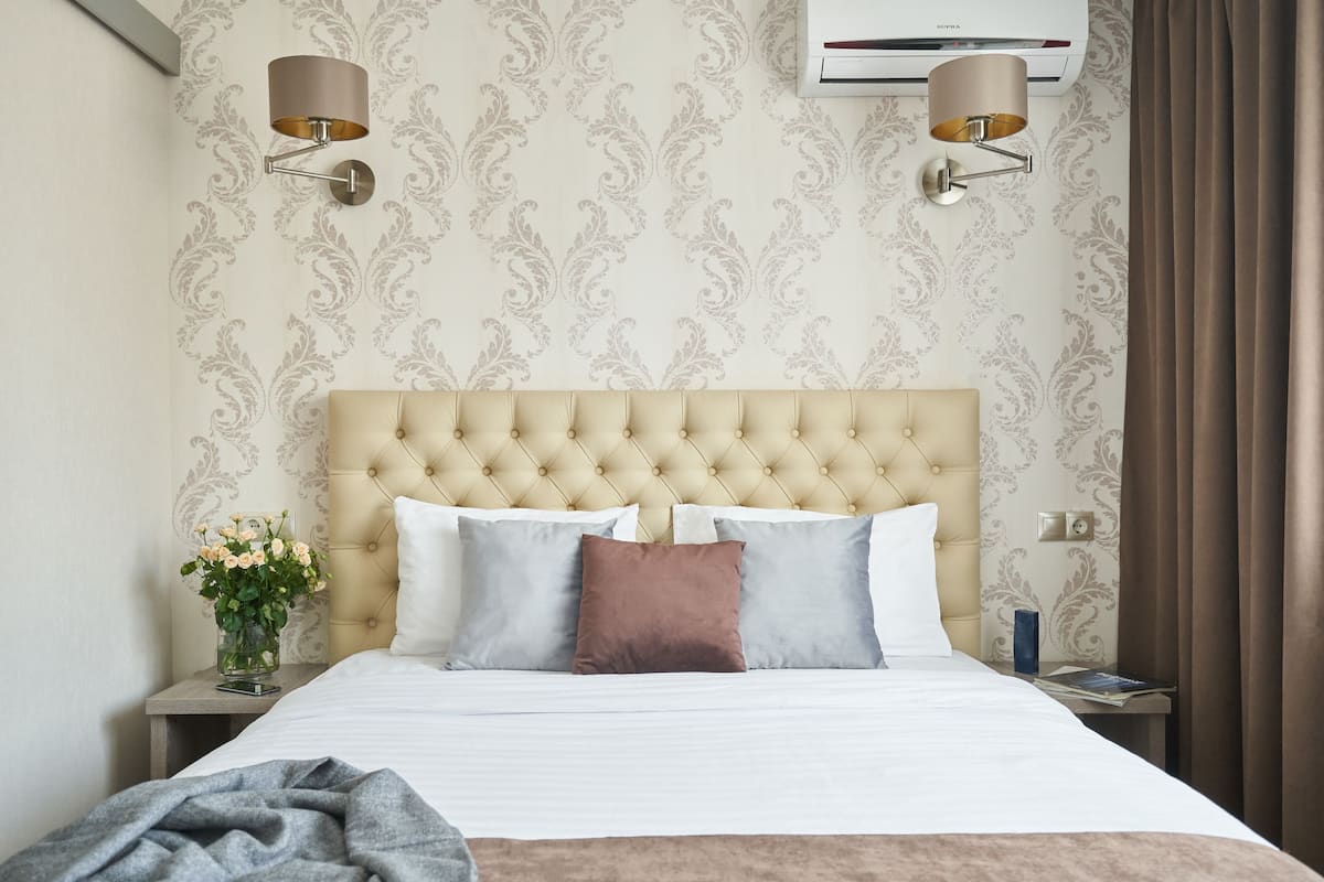 A neatly made bed with a tufted headboard, two bedside lamps, and a vase with flowers on a nightstand.