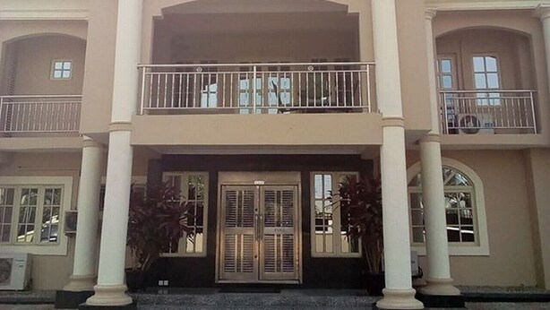 A building with a sign reading "DAVOK SUITES". It features a central entrance with double doors, flanked by columns, and a balcony on the upper floor. - Davok Suites Uyo (Uyo)