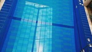 A view of a swimming pool with clear blue tiles and a glass ceiling, reflecting the sky and surrounding buildings. - Davok Suites Uyo (Uyo)