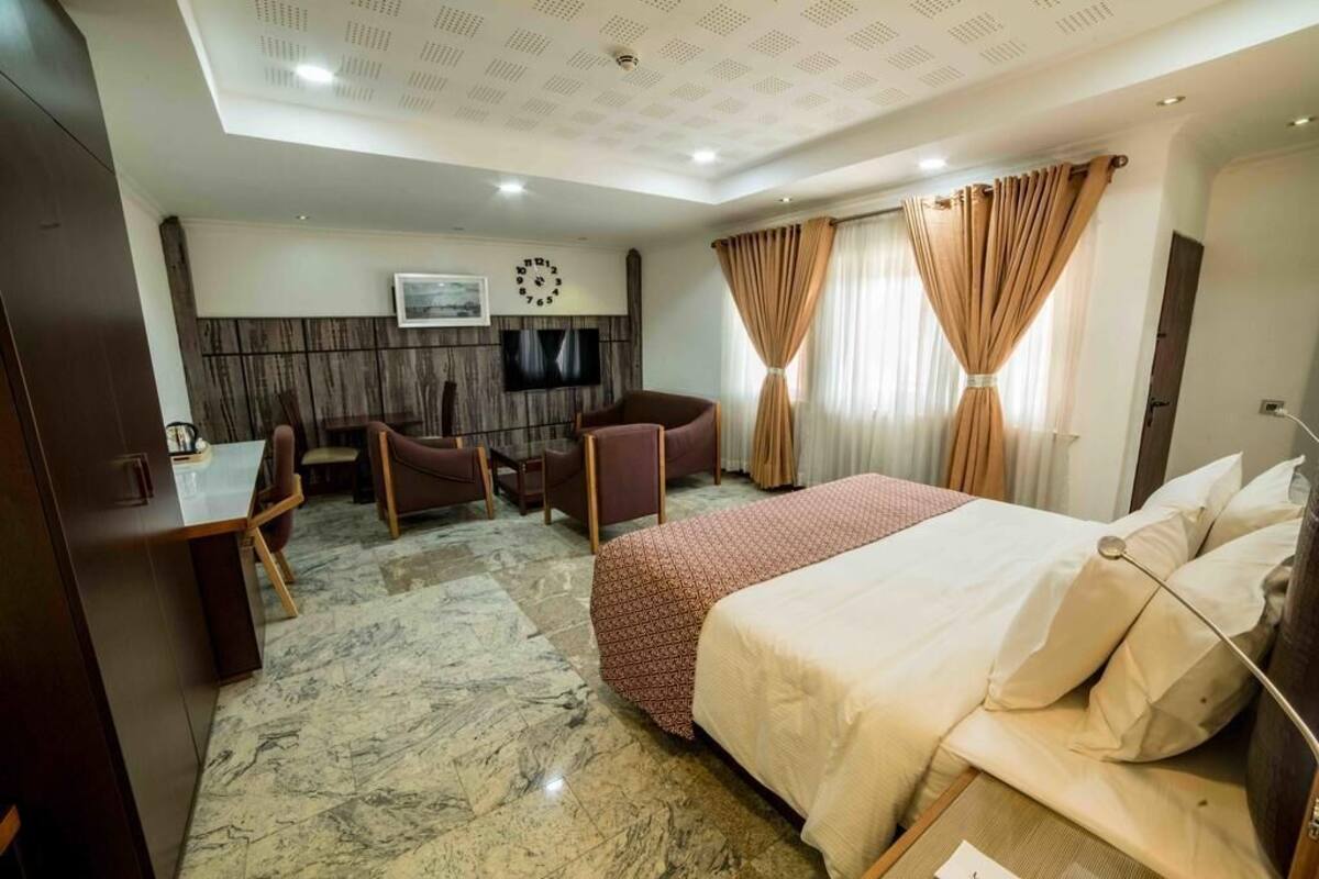 A hotel room with a bed, a desk, a chair, a television, and a clock on the wall.