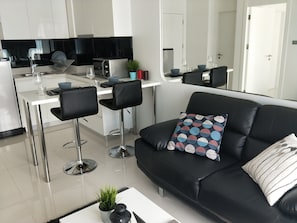 Une cuisine moderne avec un coin repas, un canapé en cuir noir et une petite table agrémentée d’une plante.