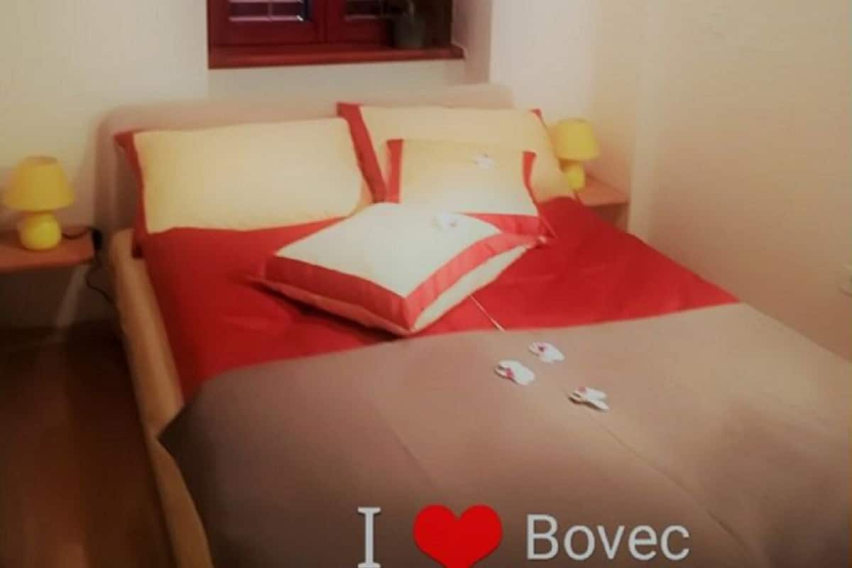 A bedroom with a bed, two bedside lamps, a window with blinds, and a wall-mounted sign.