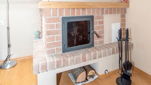A room with a brick fireplace, a wooden mantel, and a window with a view of trees.