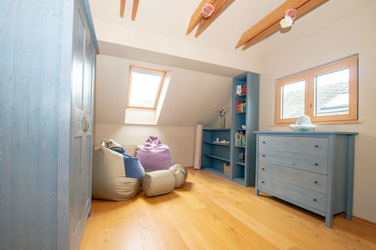 A room with a wooden floor, a blue wardrobe, a blue dresser, a window, and a skylight.