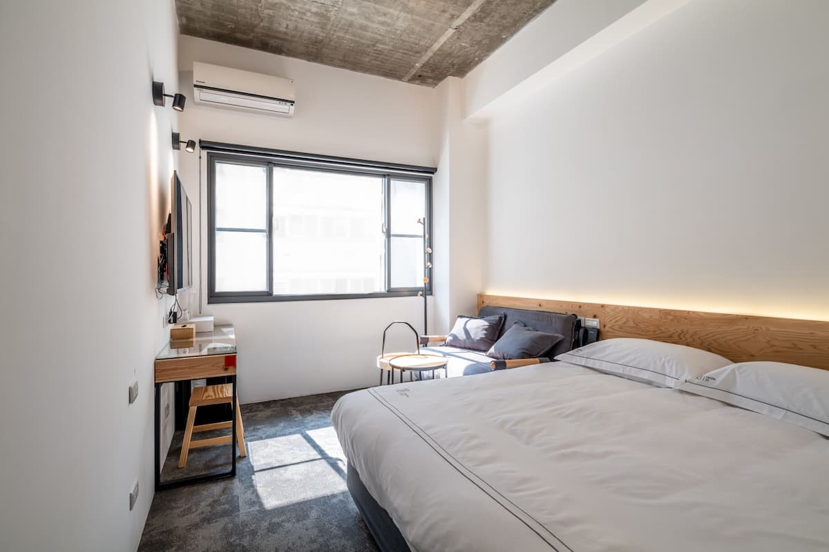 Una habitación de hotel moderna con una cama, mesita de noche y un pequeño escritorio con una silla.