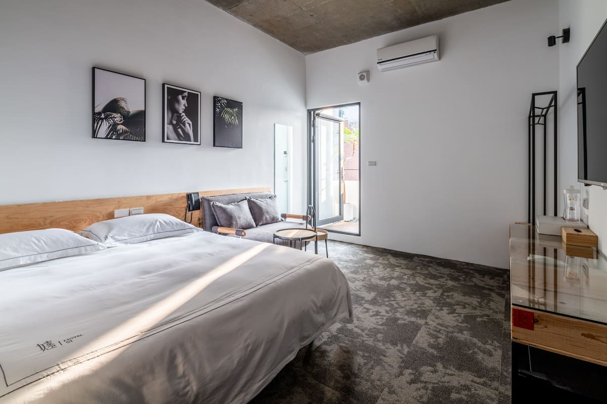 Una habitación de hotel moderna con una cama grande, una mesita pequeña y un aparador de vidrio.