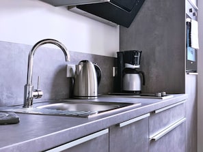 A modern kitchen with a stainless steel sink, a kettle, and a coffee maker.