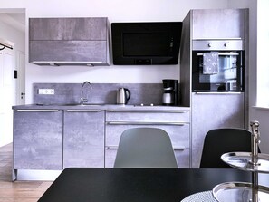 Eine moderne Küche mit grauen Schränken, einer Edelstahlspüle, einem Wasserkocher, einer Kaffeemaschine und einer Mikrowelle.
