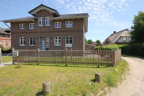 Ein Backsteinhaus mit Holzzaun, einem sichtbaren Schild und einem unbefestigten Weg.