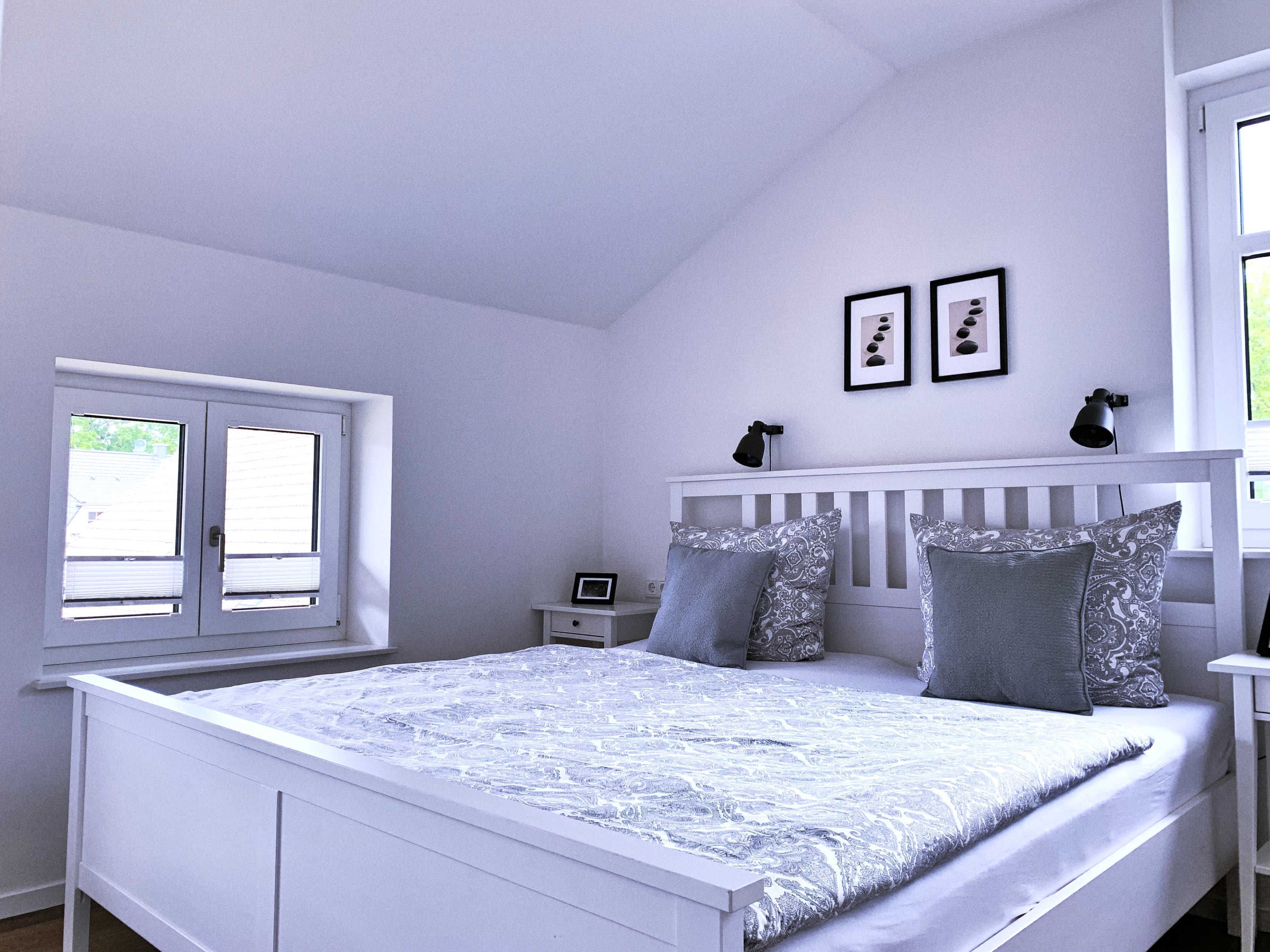 A bedroom with a bed, a nightstand, a window, and two wall-mounted lamps.