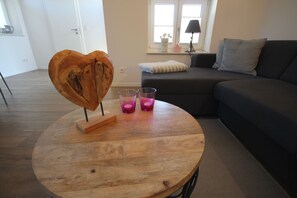 Ein runder Holztisch mit einem herzförmigen Gegenstand, zwei Gläsern und einem Sofa in einem Wohnzimmer.