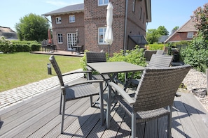 A patio with a table and chairs, a brick house in the background, and a grassy area.