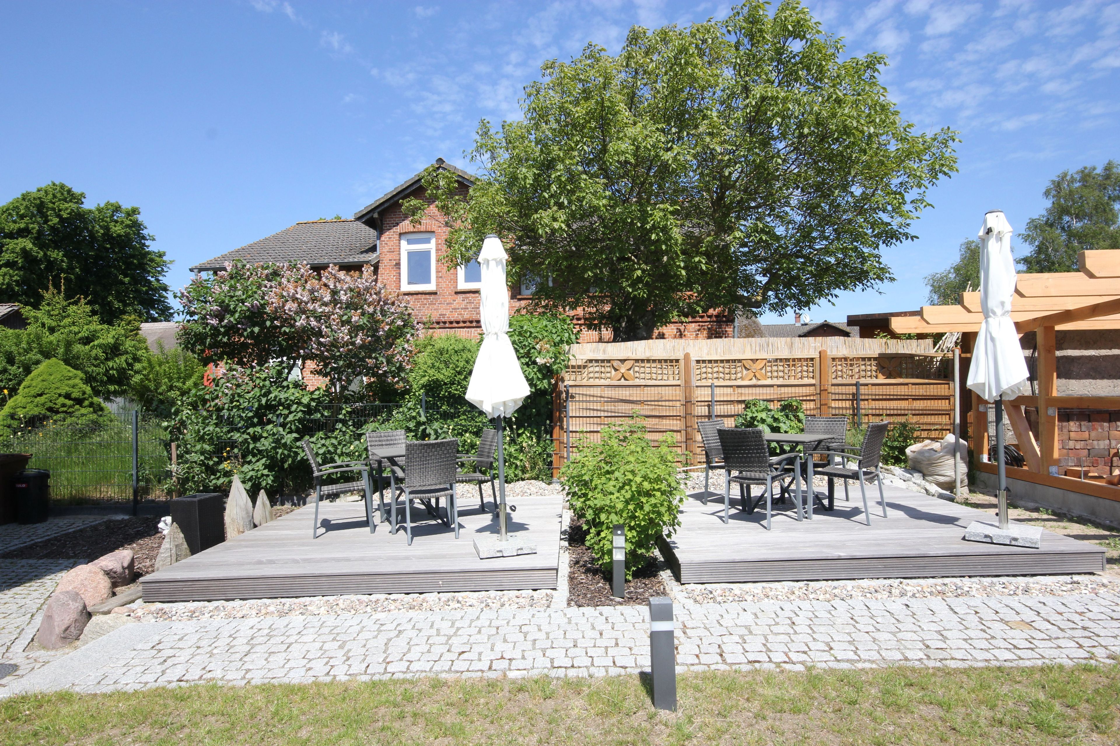 Un patio con mobiliario exterior, un pequeño jardín y una casa de ladrillo al fondo.