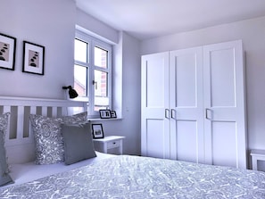 A bedroom with a bed, a nightstand, a window, and a wardrobe.